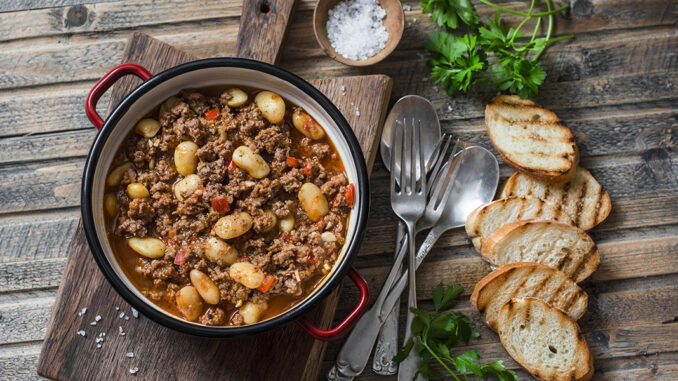 Cannellini beans beef slow-cooker stew on the wooden table, top view. Autumn, winter seasonal, healthy comfort food