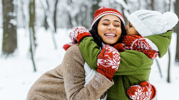 cute african american daughter hugging mother in winter forest